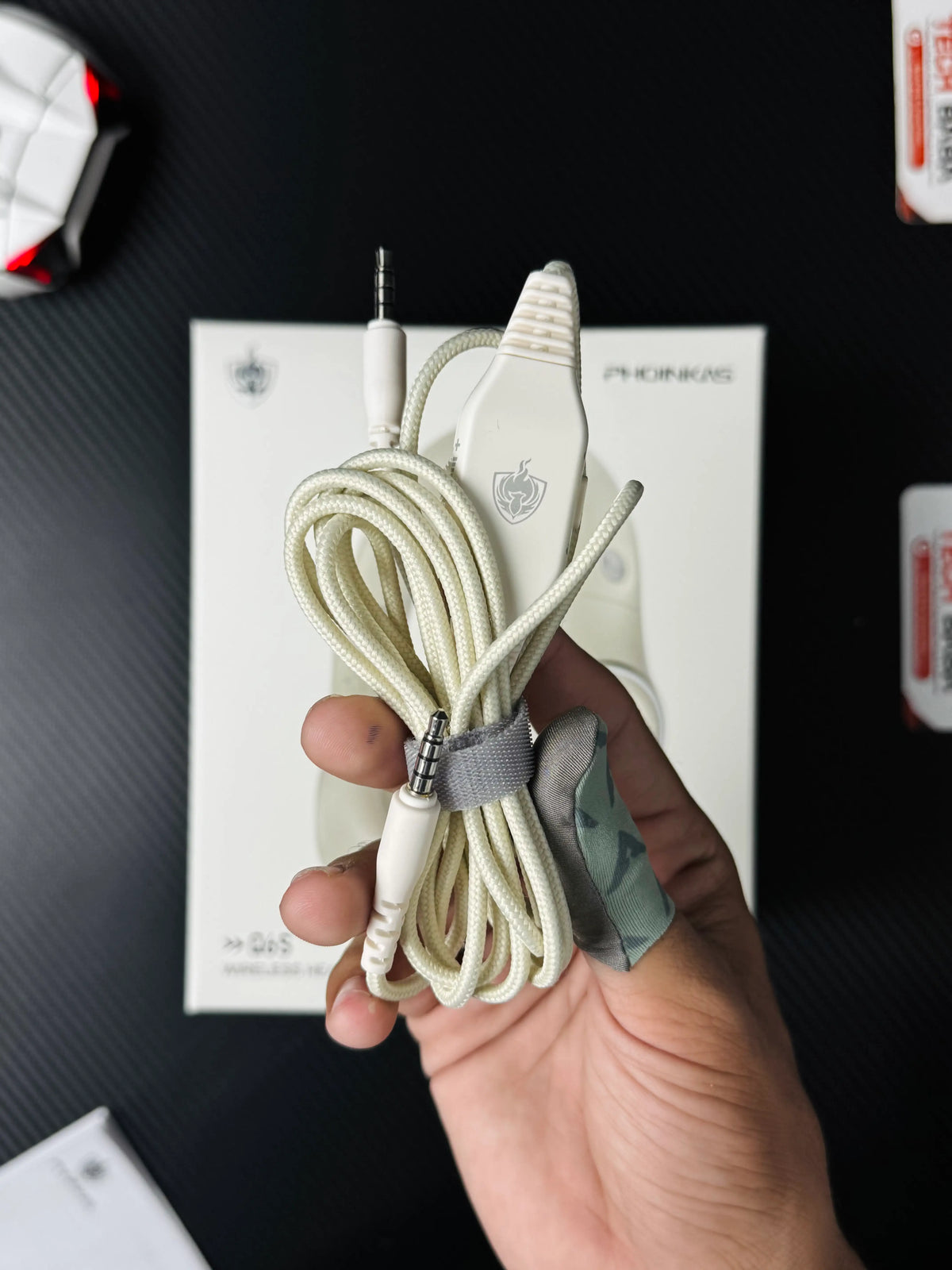 A hand holding Phoinikas Q6S Wireless Gaming Headset — Bluetooth 5.3, Detachable Mic, 30Hrs Battery | Best PUBG Headset Pakistan which has showing 3.5mm wire with volume control.picture By TechBabaStore.pk