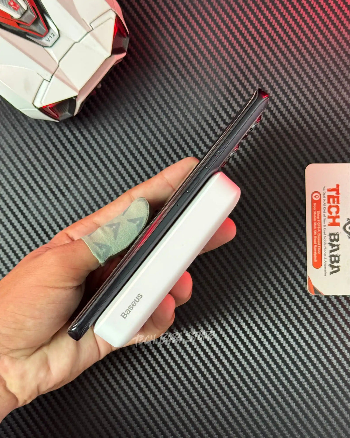 a hand holding a motorola android phone which is wirelessly charging with Baseus PPCXM10 Wireless PowerBank and showing side closeup view and also showing Baseus label. picture by TechBabaStore.pk