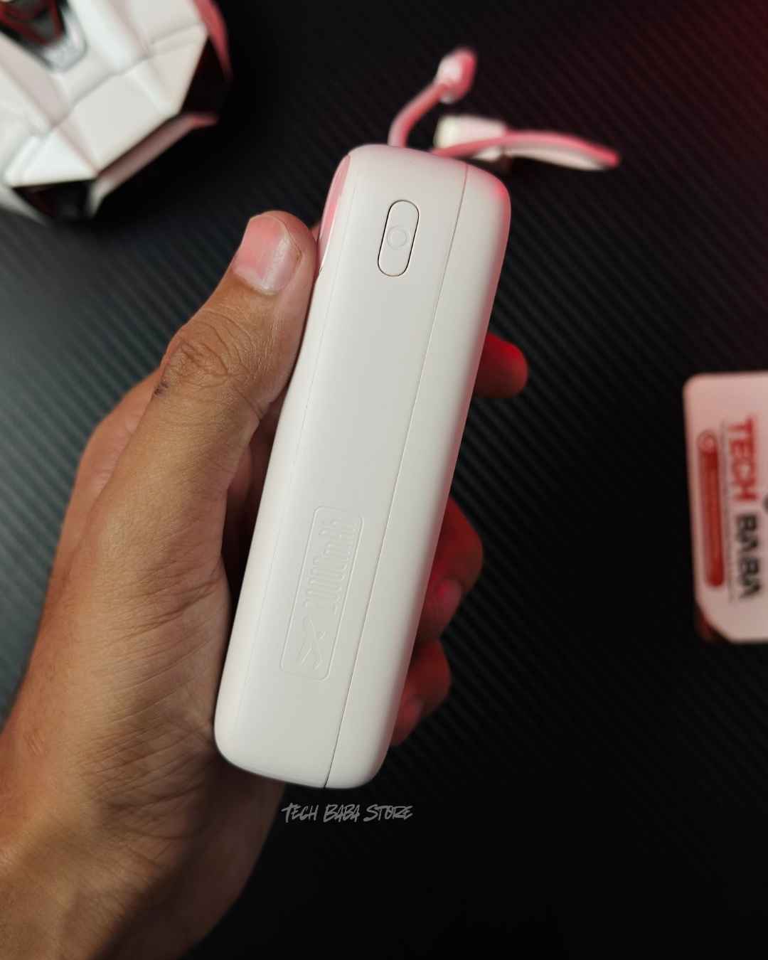 A hand holding a pink colour Baseus Enerfill FC11 20000mAh 22.5W Power Bank showing side view that has a power button - Picture by TechBabaStore.pk