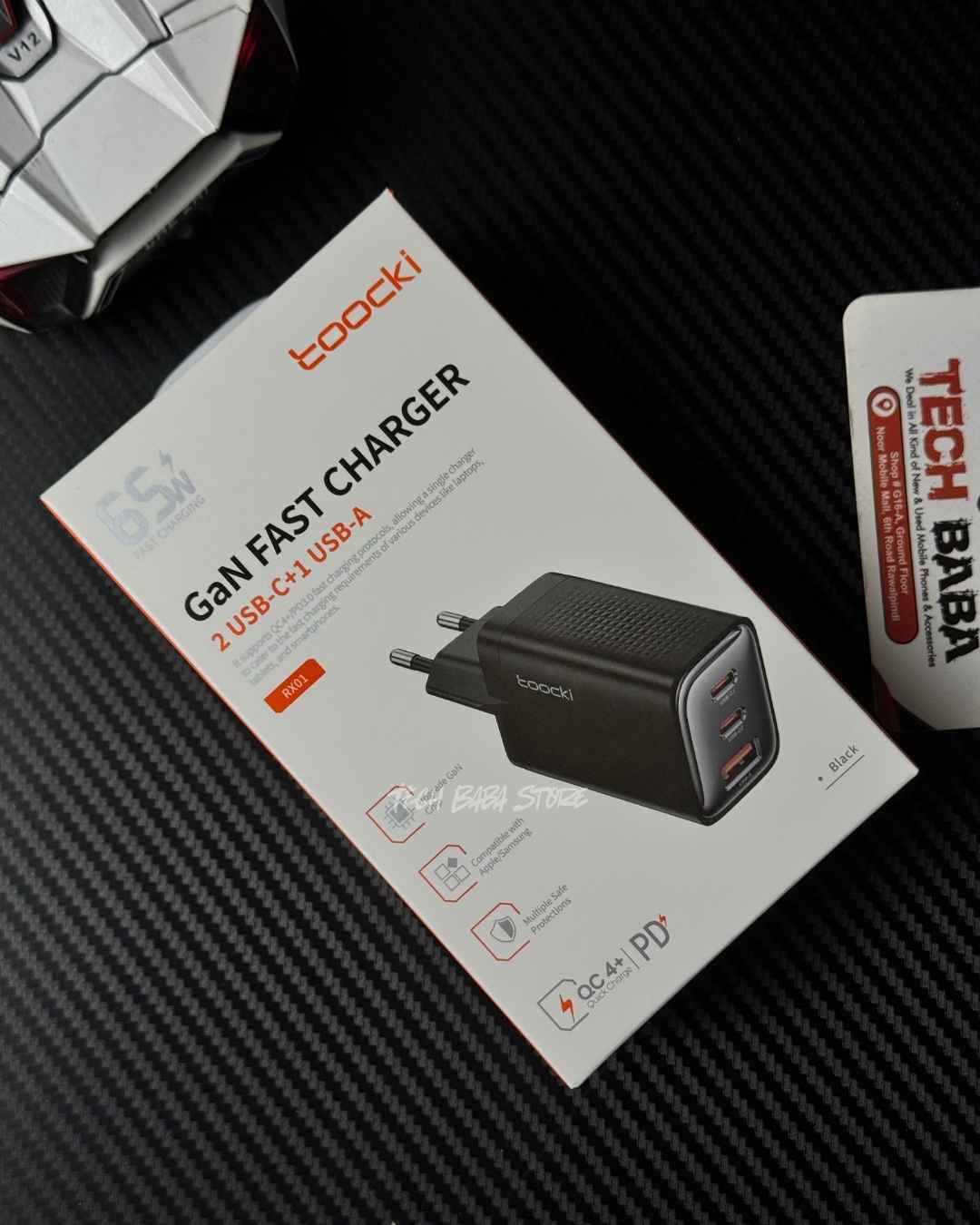 A Toocki RX-01 65W GaN fast charger 2 USB-C 4 USB-A adapter shown next to its white retail packaging box on a black textured surface.