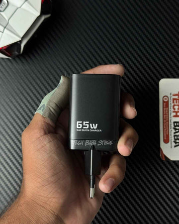 A hand holding a Toocki black 65W GaN quick charger adapter with a USB-C plug, set against a dark carbon fiber textured background.