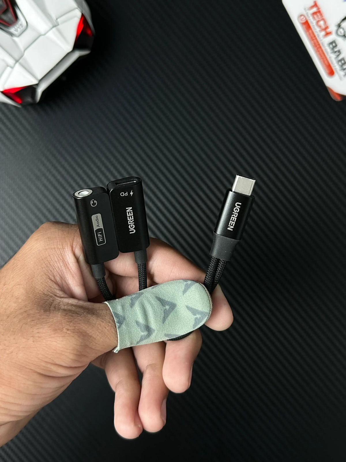 A hand holding UGREEN 25837 USB-C to 3.5mm Audio Adapter Pakistan which has showing all type of wires picture by .TechbabaStore.pk