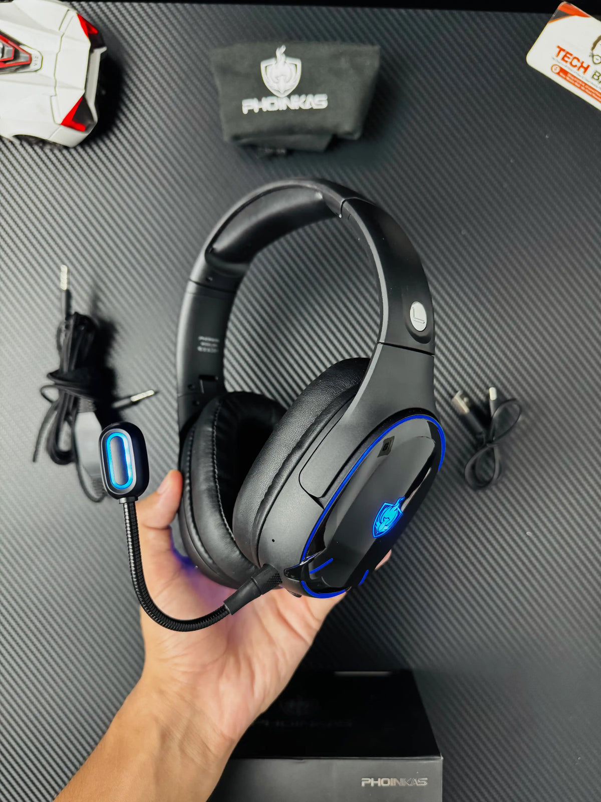 A hand holding Phoinikas Q6S Wireless Gaming Headset — Bluetooth 5.3, Detachable Mic, 30Hrs Battery | Best PUBG Headset Pakistan  which has showing black headset with light. picture By TechBAbaStore.pk