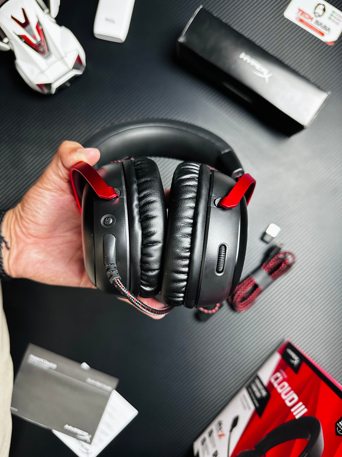 A hand holding HyperX Cloud III Gaming Headset for PUBG Mobilewhich has showing button and contol.picture by TechBabaStore.pk