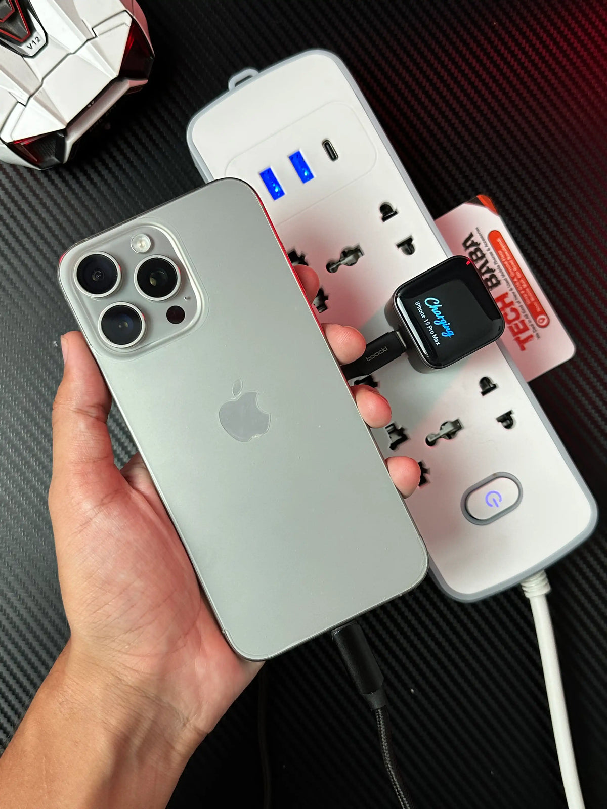 A hand holding iphone 15 pro man which has showing in nker_Nano_45W_Charger_With_Smart_Display on display charging iphone 15 pro max.picture by TechBabaStore.pk