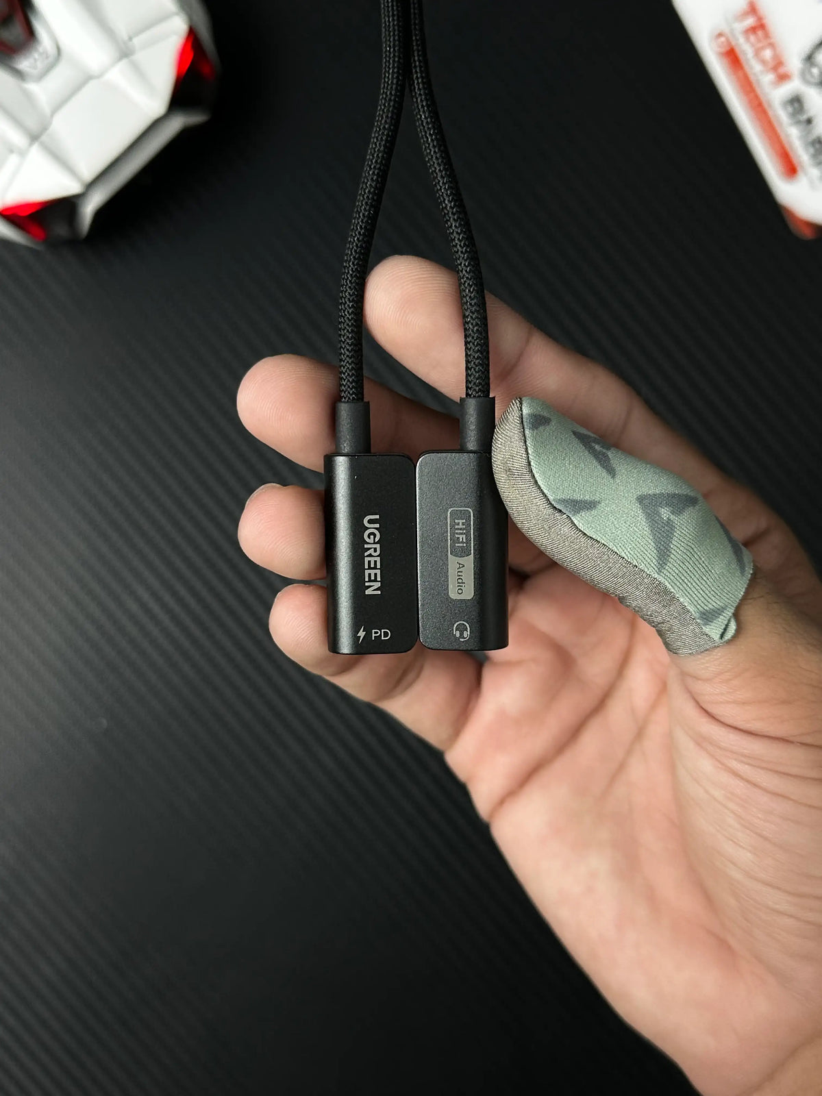 A hand holding UGREEN 25837 USB-C to 3.5mm Audio Adapter Pakistan which has showing connector .picture by TechBabaStore.pk