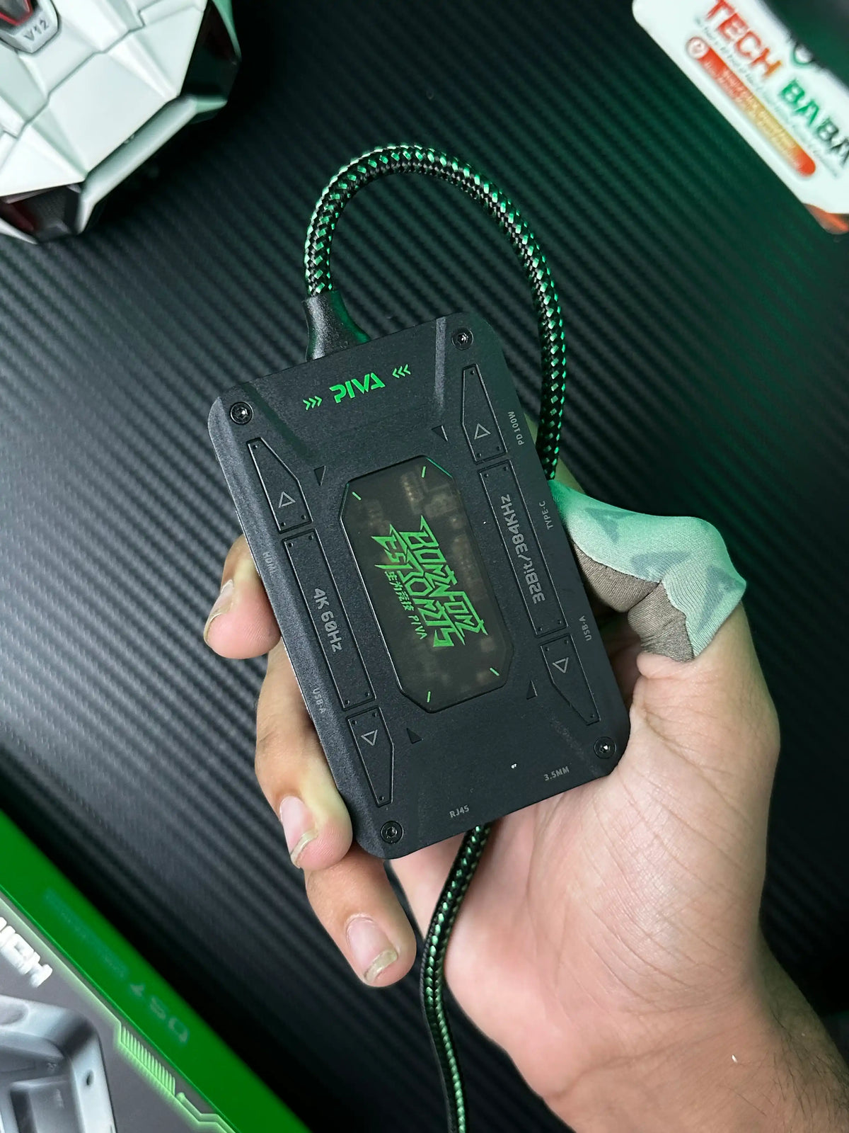 A hand holding Piva DS7 7-in-1 Gaming Splitter — Ethernet, 100W PD, 4K HDMI for PUBG Mobile which has showing front side view of Piva DS7 7-in-1 Gaming Splitter — Ethernet, 100W PD, 4K HDMI for PUBG Mobile.picture by TechBabaStore.pk