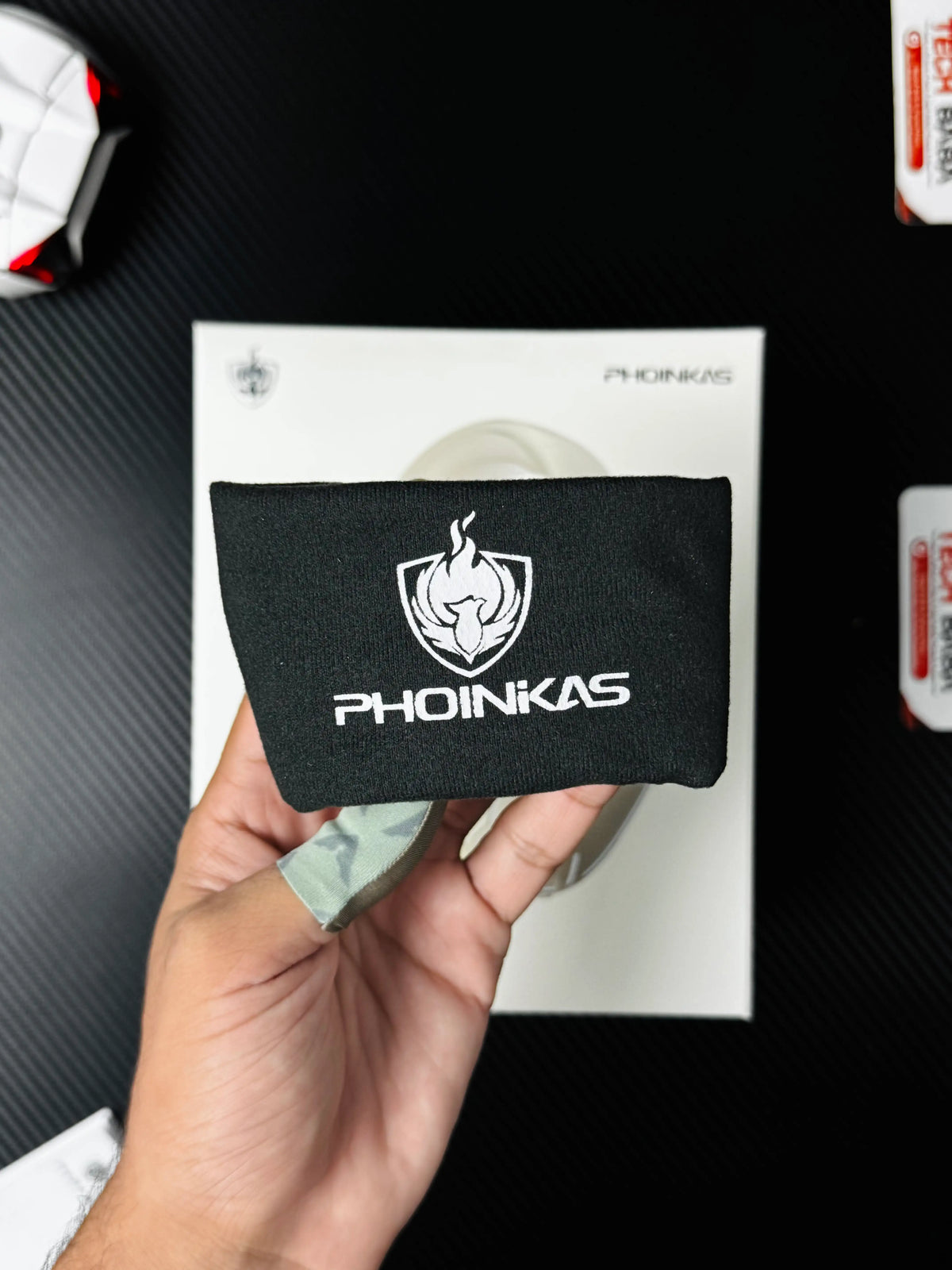A hand holding Phoinikas Q6S Wireless Gaming Headset — Bluetooth 5.3, Detachable Mic, 30Hrs Battery | Best PUBG Headset Pakistan bag which has showing black bag with label. picture by TechBabaStore.pk