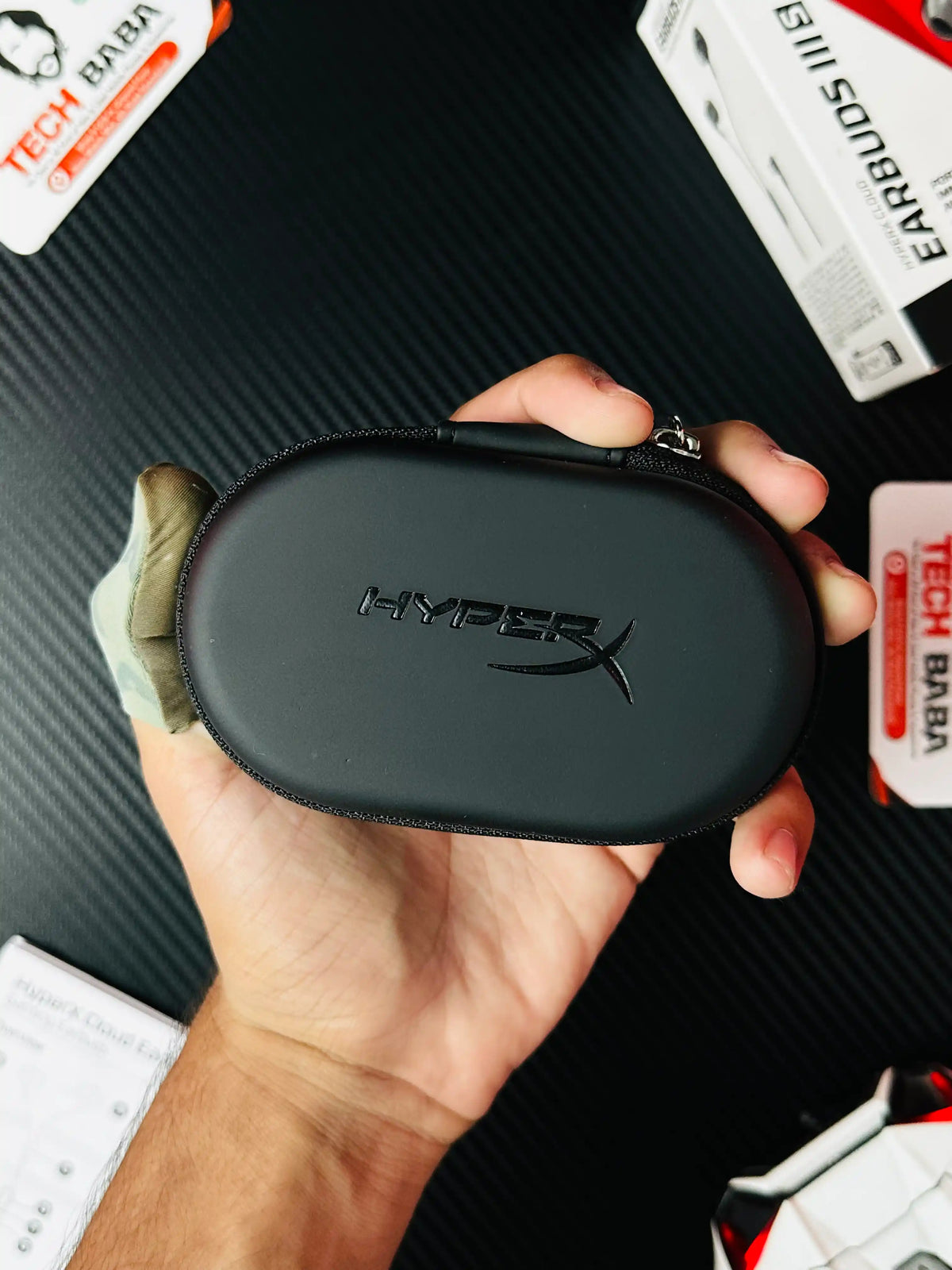 a hand holding small pouch of HyperX Cloud Earbuds III S USB-C Gaming Earbuds which has showing label of hyoperx -picture by TechBabaStore.pk