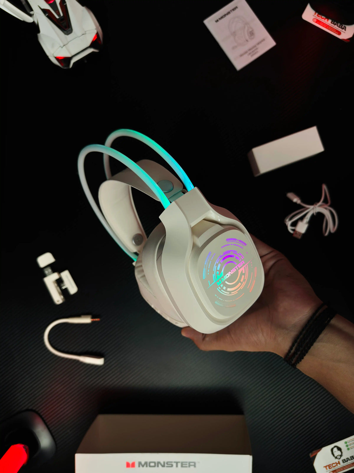 A hand holding Monster_Maxstar_MQH09_Wireless_Gaming_Headphone_50mm_Driver_Bluetooth_5.4_IPX5_Best_PUBG_Headset_Pakistan which has showing label of monster and all things with lighs picture by TechBabaStore.pk