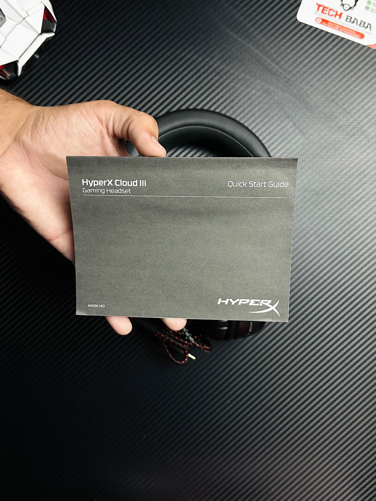 A hand holding HyperX Cloud III Gaming Headset for PUBG Mobile  which has showing quick start guide 
.picture by TechBabaStore.pk