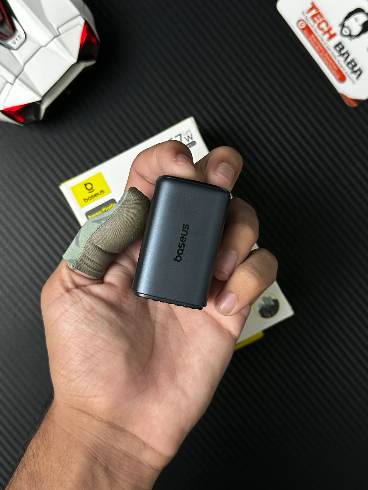 A hand holding Baseus_PicoGo_AE11_67W_GaN_Fast_Charger_2C_U_Dual_USB-C_USB-A_PD3.0_QC4.0_PPSwhich has showing label of baseus.picture by TechBabaStore.pk