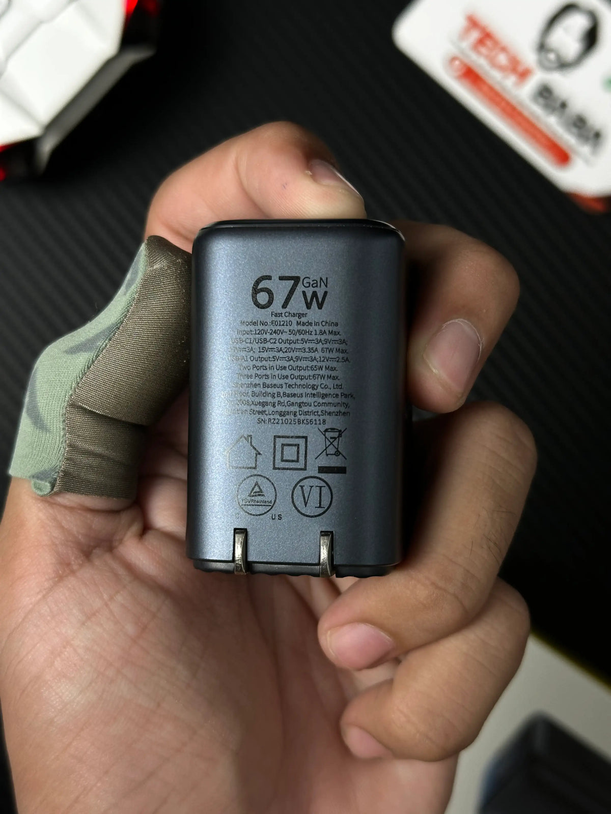 A hand holding Baseus_PicoGo_AE11_67W_GaN_Fast_Charger_2C_U_Dual_USB-C_USB-A_PD3.0_QC4.0_PPS_which has showing specification.picture by TechBabaStore.pk