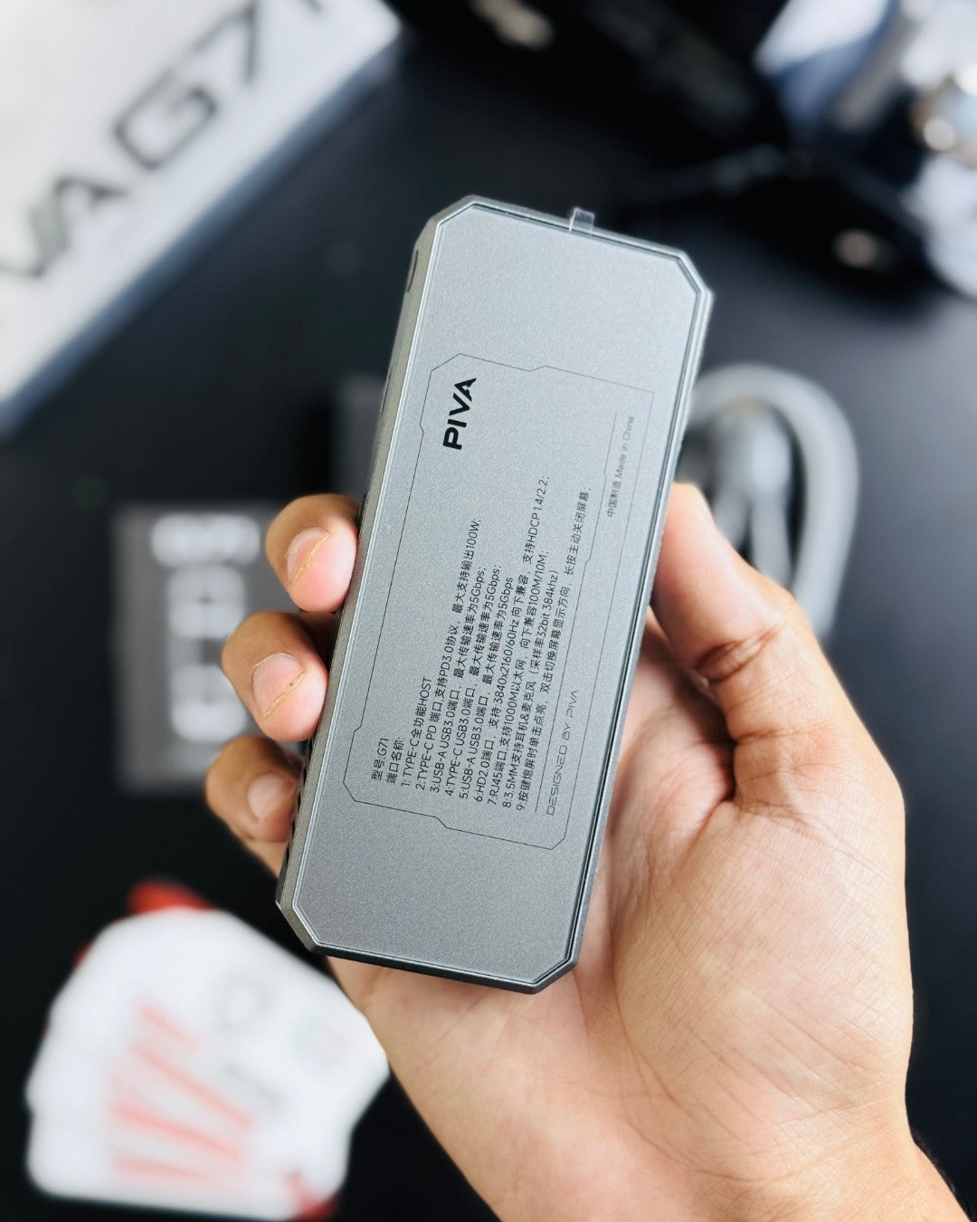 a hand holding PIVA_G71_7-in-1_Gaming_Splitter_Docking_Station which has showing specification_picture by TechBabaStore.pk