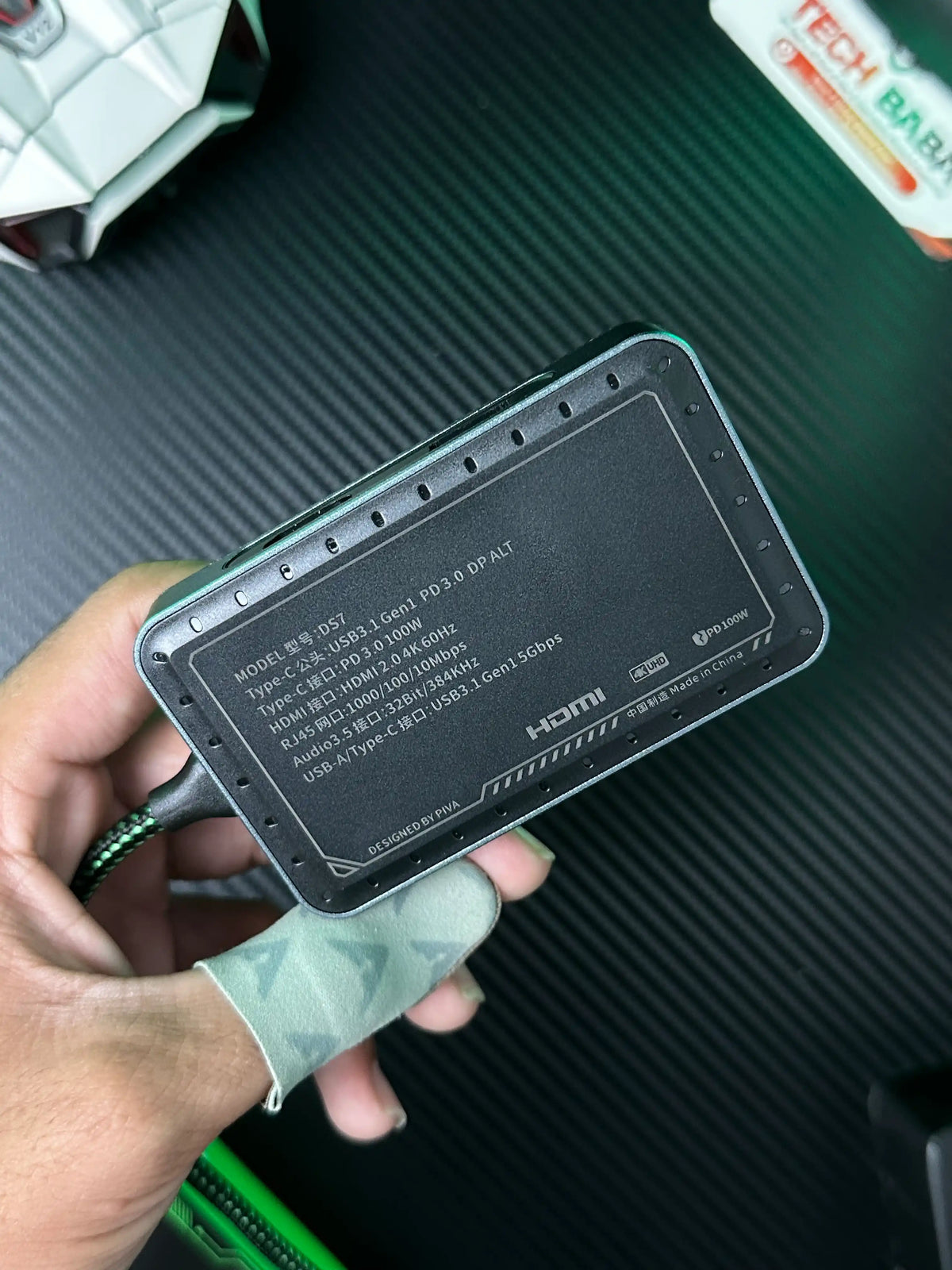 A hand holding Piva DS7 7-in-1 Gaming Splitter — Ethernet, 100W PD, 4K HDMI for PUBG Mobile which is showing speification of Piva DS7 7-in-1 Gaming Splitter — Ethernet, 100W PD, 4K HDMI for PUBG Mobile.picture by TechBabaStore.pk