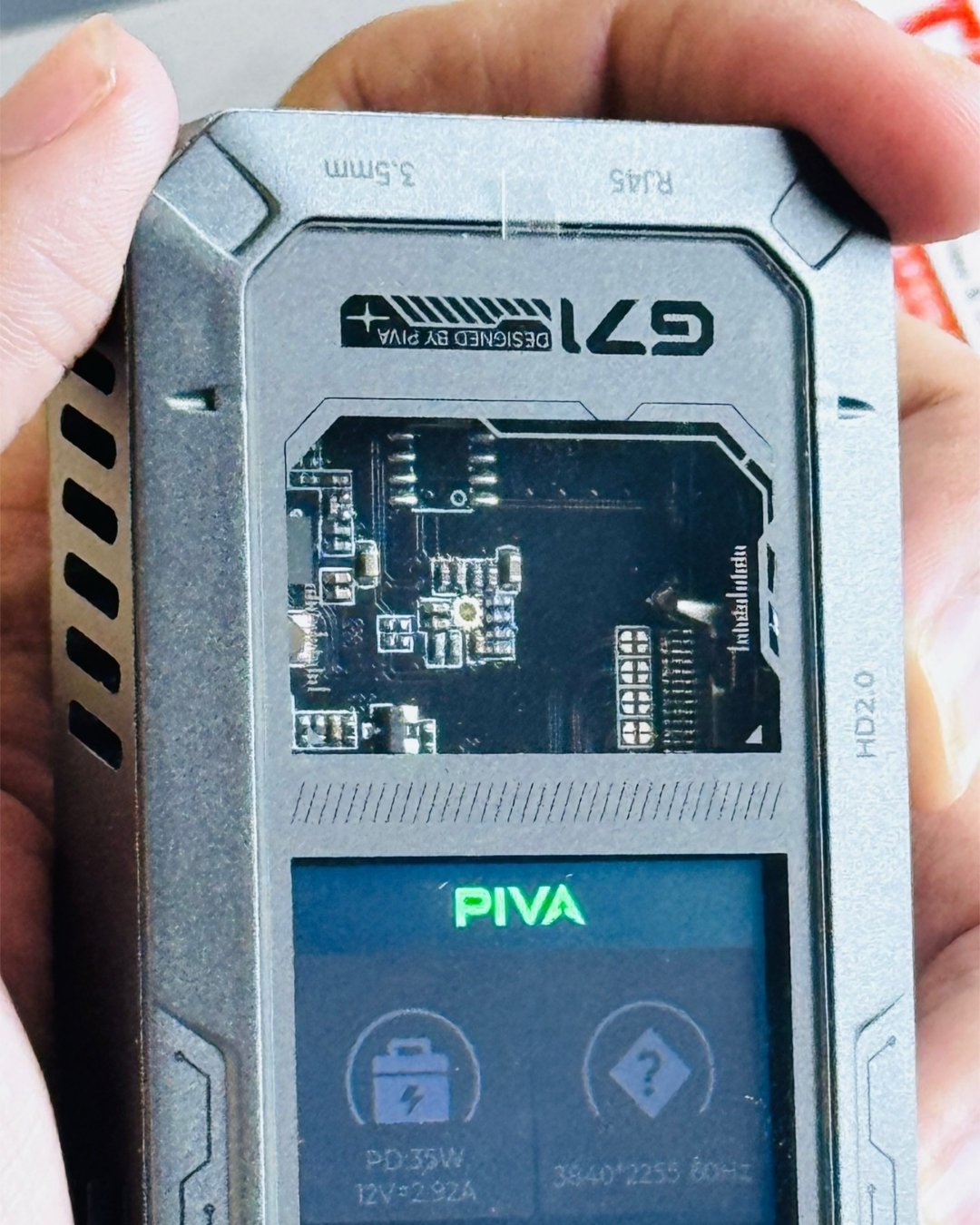 a hand holding PIVA_G71_7-in-1_Gaming_Splitter_Docking_Station which has showing transparent and dispaly_ picture by TechBabaStore.pk