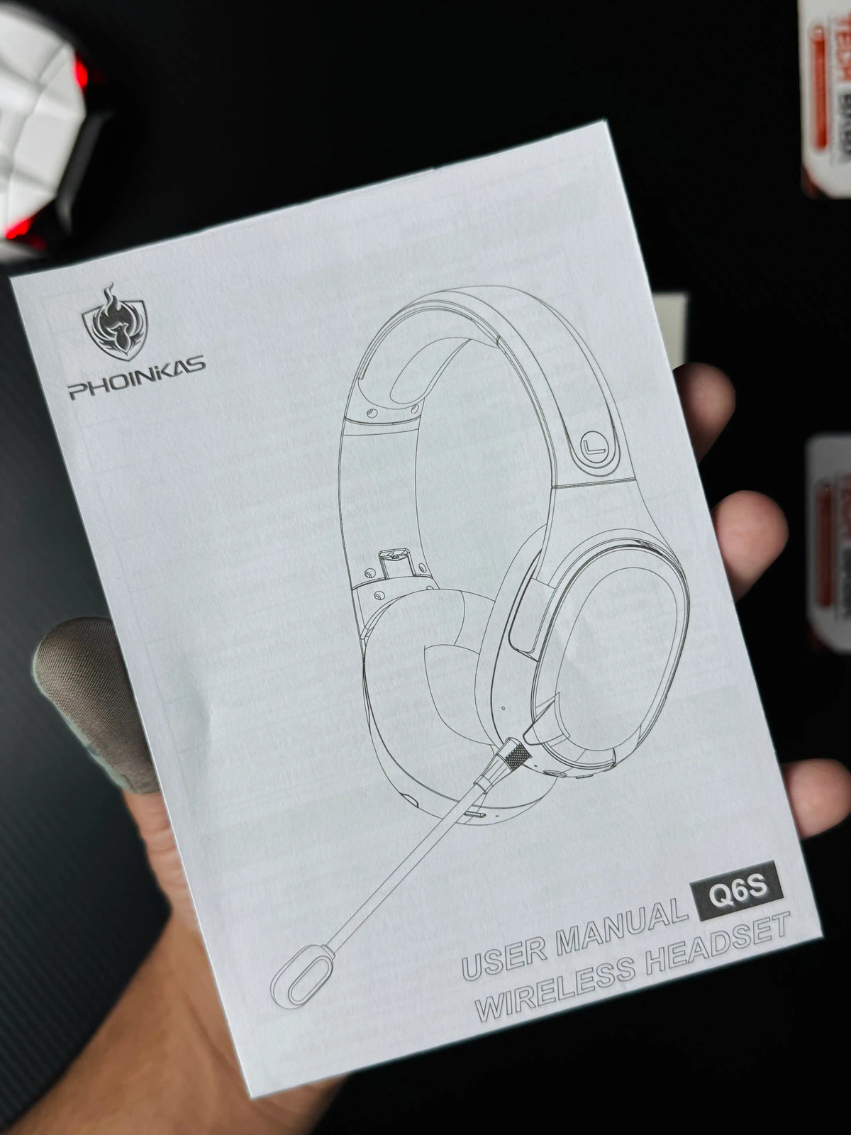A hand holding Phoinikas Q6S Wireless Gaming Headset — Bluetooth 5.3, Detachable Mic, 30Hrs Battery | Best PUBG Headset Pakistan  which has showing user manual. picture by TechBabaStore.pk